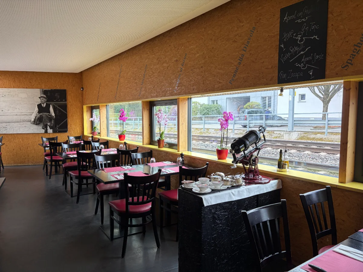 Innenansicht eines Restaurants mit Tischen und Stühlen vor einer Bar.