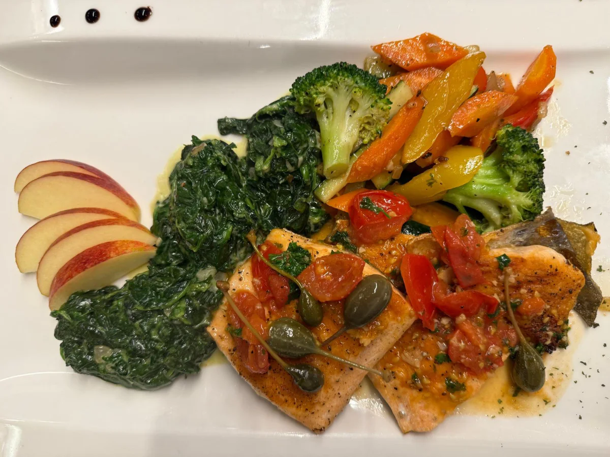 Ein Teller mit gebratenem Fisch, goldenen Kartoffeln und einer frischen Orangenscheibe.