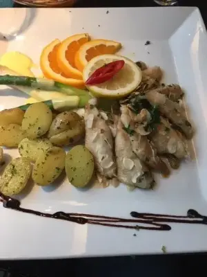 Ein Teller mit gebratenem Fisch, goldenen Kartoffeln und einer frischen Orangenscheibe.